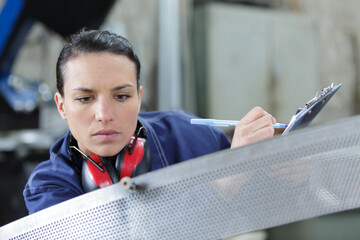 woman with clipboard inspecting industrial metal component