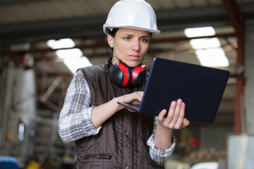 female industrial engineer uses laptop computer while standing in factory