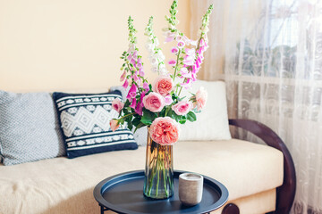 Fototapeta na wymiar Fresh bouquet of roses and foxgloves flowers put in vase in living room. Interior and home decor. Pink orange blooms
