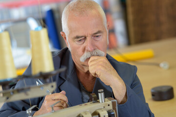 pensive senior man using industrial sewing machine