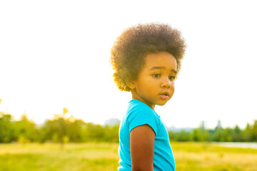 cute little african american girl in cotton blue t-shirt in spring park at sunset curly hair