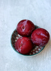 Plums on light grey background with copy space. Simple still life with seasonal fruit on a table. Eating fresh concept. 