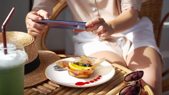 Young woman taking photo of dessert with smart phone for social media in restaurant while traveling