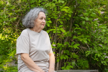 Sad lonely old woman reflects on outdoor life. Wrinkles on the face, gray hair. Retirement age.