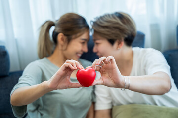 Two asian women lgbtq lesbian homosexual Lesbian couples holding red heart together in living room....