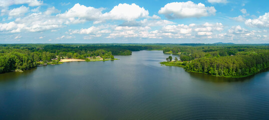 Obraz na płótnie Canvas a stunning aerial panoramic of the rippling blue waters of Lake Acworth surrounded by lush green trees, grass and plants with powerful clouds at sunset at South Shore Park in Acworth Georgia USA