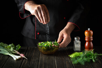 The chef adds salt to fresh lettuce salad. Cooking vegetarian food in the kitchen. Menu for a restaurant or hotel.