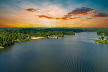 Fototapeta na wymiar a stunning aerial shot of the vast blue rippling waters of Lake Acworth surrounded by lush green trees, grass and plants with powerful clouds at sunset at South Shore Park in Acworth Georgia USA