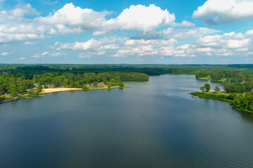 Obraz na płótnie Canvas a stunning aerial shot of the vast blue rippling waters of Lake Acworth surrounded by lush green trees, grass and plants with blue sky and powerful clouds at South Shore Park in Acworth Georgia USA