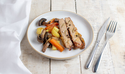 Sliced roasted pork meat in plate with vegetables on wooden table with rosemary and peppers.