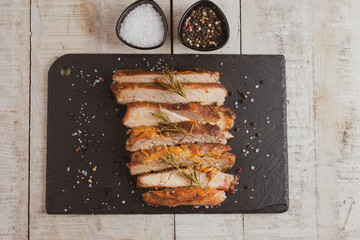 Roasted sliced pork meat in stone plate with spices on wooden background