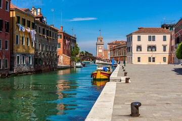 Street along canal and colorful houses in Venice, Italy.