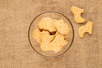 Several homemade zoological cookies in glassware on jute fabric, close-up, top view.
