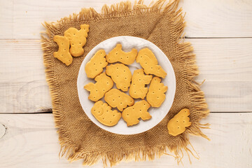 Several zoological cookies with a ceramic saucer and a jute napkin on a wooden table, macro, top view.