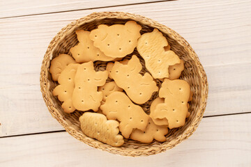 Several zoological cookies in a straw plate on a wooden table, macro, top view.