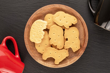 Several homemade zoological cookies with a wooden saucer and two cups on a slate stone, close-up, top view.