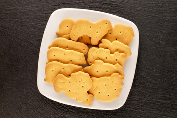 Several homemade zoological cookies with a white ceramic saucer  on a slate stone, close-up, top view.