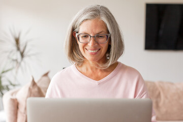 Happy stylish mature old woman remote working from home distance office on laptop