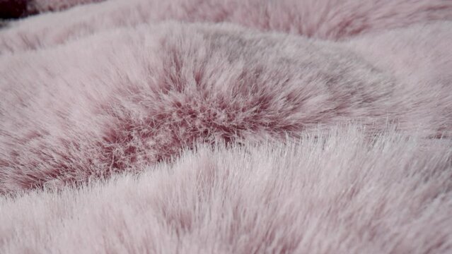 Texture of soft fluffy pink fur fabric. Faux hairy fur. Fluffy fake fur clothes, furry blanket. The camera moves along the hairs of fur. Textile shaggy fiber close up. Fashion industry textile.