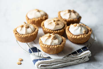 Lemon curd tartlets with whipped meringue on a wire rack on a gray background.