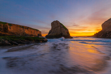 Fototapeta na wymiar Sunset behind rocks with waves crashing on Santa Cruz beach