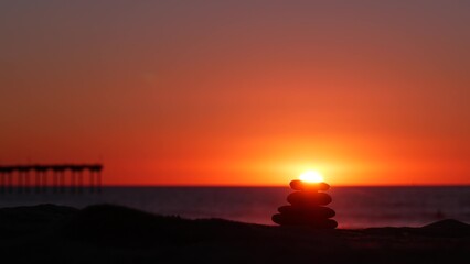 Stack of pebble stones, sandy ocean beach, sunset sky. Rock balancing in sun light, sea water waves. Stones staking in pyramid pile. Zen meditation and harmony in balance. Seamless looped cinemagraph.