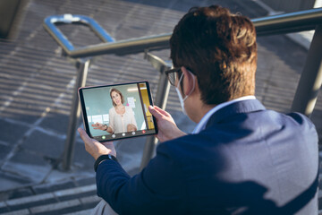 Asian businessman video calling caucasian female colleague through digital tablet outside office