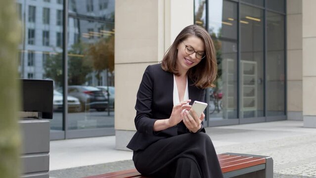 Business woman sitting on bench using smartphone