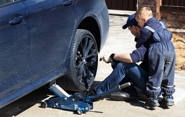 Father and son are fixing the car. The son helps the dad. Happy Father's Day.