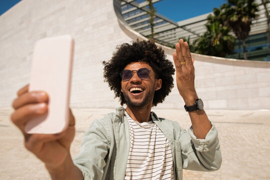 Jokey African American man taking selfie outdoors. Man in casual shirt with beard holding mobile phone, taking pictures. Social media, technology concept