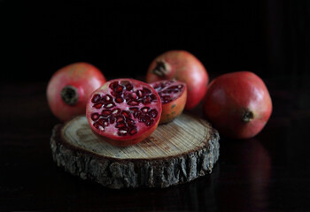 Pomegranate and its slices on chopping plate on dark background. 