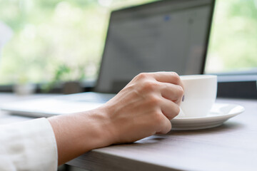 Closeup shot of hand woman working and holding mug coffee. Beautiful woman break time in modern office. Concept of business, technology, coffee break and meeting online.