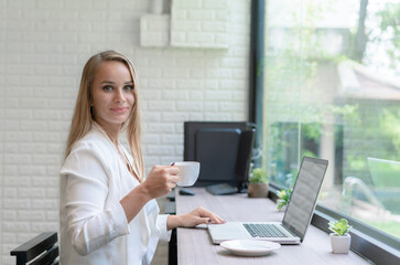 Business caucasian woman working and holding mug coffee. Beautiful woman break time in modern office. Concept of business, technology, coffee break and meeting online.