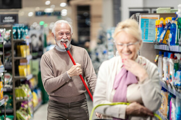 Playful senior couple playing and acting like singer in supermarket.