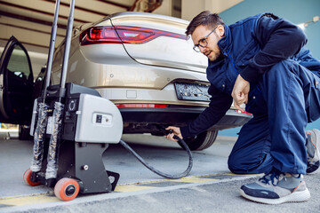 A car service worker checking on exhaust gases on a car in garage.