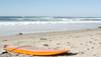Surfboard for surfing lying on beach sand, California coast, USA. Ocean waves and orange surf board...