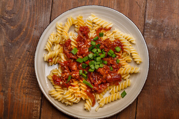 Plate with bolognese pasta on a wooden table sprinkled with green onions.