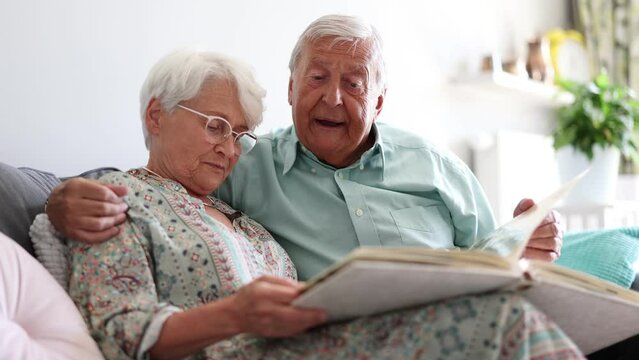 Elderly couple looking at a photo album while sitting on a sofa
