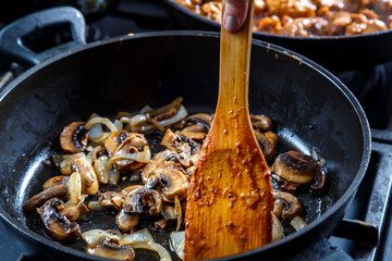 Mushrooms fried with onions in a deep frying pan with a wooden spatula.
