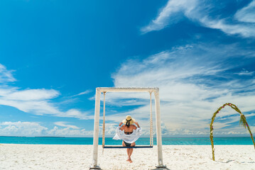Young woman with hat on a swing in front of beautifull Indian Ocean tropical beach. Zanzibar...