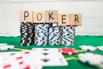The word poker on wooden cubes, poker chips with playing cards on the green casino table.