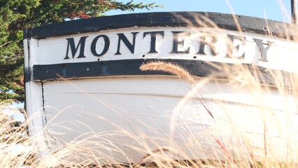 Monterey sign on white wooden boat stern, fisherman nautical vessel stem, bow or rostrum near Cannery Row and Bay Aquarium. Coniferous pine cypress tree. Historic capital, tourist city, California USA