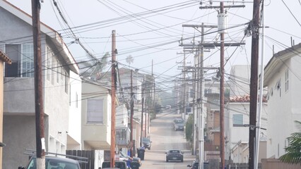 Power lines or wires on poles, foggy city street, California, USA. Cables on high voltage wooden electricity posts or pylons in misty San Diego. Power supply and houses in America. Cloudy weather.