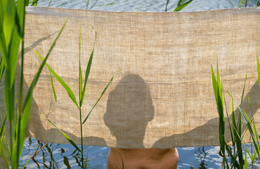 Hemp towel in men's hands. After swimming. A man holds a canvas against the sun. Silhouette of a man on a cloth.