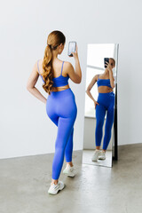 Portrait of young proud muscular woman boasting her fit figure and slim waist taking sefie in gym...