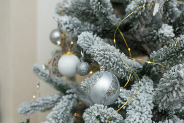 Fototapeta na wymiar fir tree branches covered with artificial snow, white and silver bulbs, baubles, golden garlands. Christmas tree closeup
