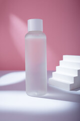 Transparent toner bottle on pink backdrop in harsh light mockup, no brand template. Korean care cosmetics container, copy space