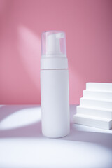 White dispenser mockup on pink backdrop in harsh light, no brand template. Cleansing moisturizing facial foam container, concrete stairs
