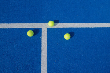 three padel tennis balls on a blue court