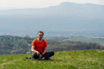 Naklejka na ściany i meble Young smiling man sitting on the mountain peak